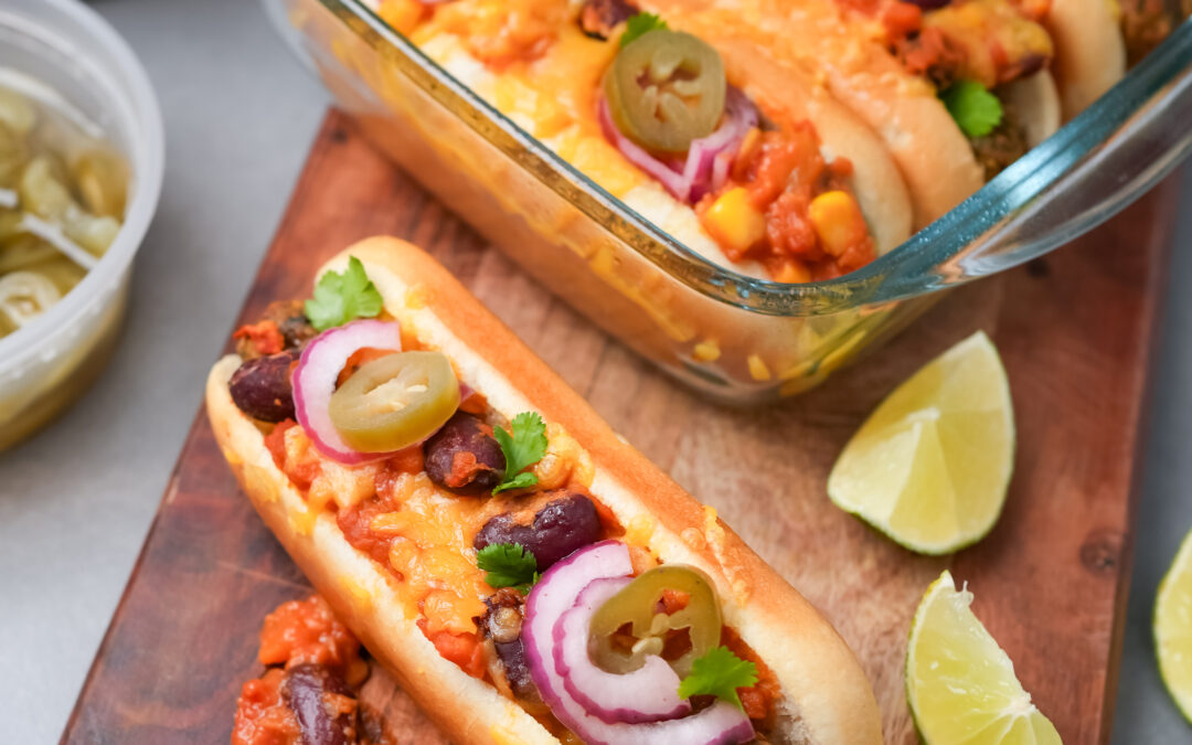 Vegetarische Chili Dogs auf Holzbrett mit Limettenspalten und eingelegten Jalapeños