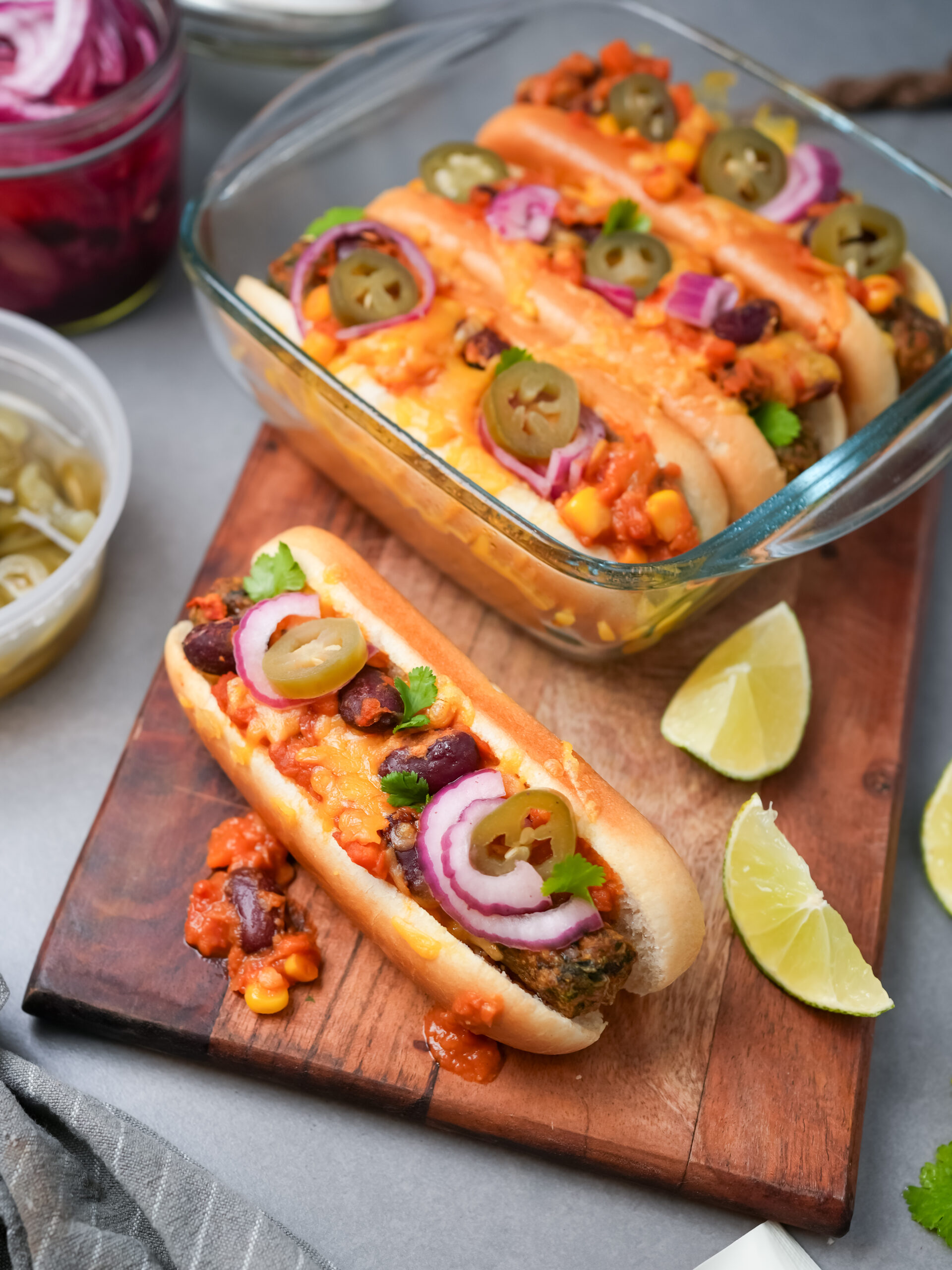 Vegetarische Chili Dogs auf Holzbrett mit Limettenspalten und eingelegten Jalapeños